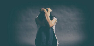 A person sitting on the floor with their arms wrapped around their knees, conveying a sense of distress