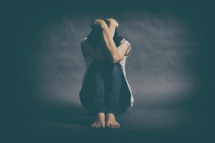 A person sitting on the floor with their arms wrapped around their knees, conveying a sense of distress