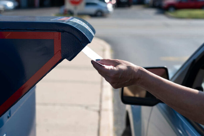 A hand inserting a letter into a blue mailbox
