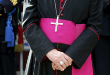 Chilling Threats Target Catholic School A bishop in traditional attire with a cross necklace and a pink sash, hands clasped in front