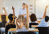 Denver Classroom Kissing Skits Exposed Children in a classroom raising their hands to answer a question while a teacher stands in front