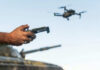 Person controlling a drone with a remote while a tank is in the background