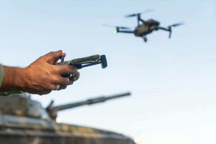 Person controlling a drone with a remote while a tank is in the background
