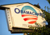 Sign displaying Obamacare with a blue and red logo against a clear sky