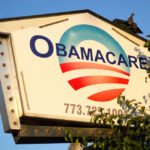 Sign displaying Obamacare with a blue and red logo against a clear sky