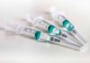 Three syringes filled with blue-green liquid on a white surface