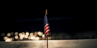 A small American flag positioned in front of the word 'PENTAGON' on a reflective surface
