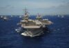 An aircraft carrier surrounded by various naval ships in the ocean