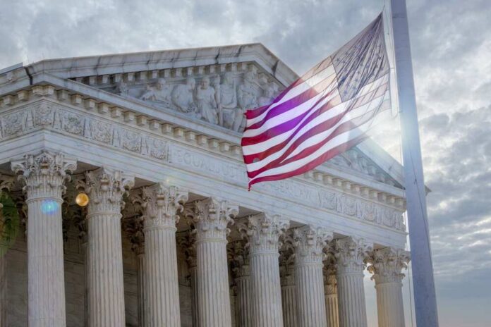 The,Sun,Peaks,Through,Clouds,To,Stream,Through,American,Flag The Supreme Court building with an American flag waving in front