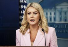 A woman in a pink blazer speaking at a podium during a press briefing