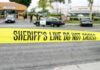 yellow sheriff's line tape blocks a street near police cars