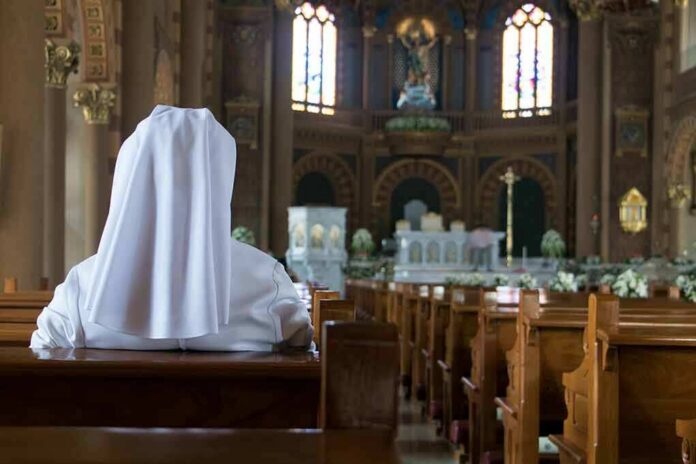 shutterstock_1016805721 Person in white habit seated in a church pew facing the altar