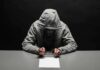 Anonymous Tip Unmasks Chilling Teen Plan Person in gray hoodie writing while handcuffed at a table