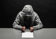 Anonymous Tip Unmasks Chilling Teen Plan Person in gray hoodie writing while handcuffed at a table