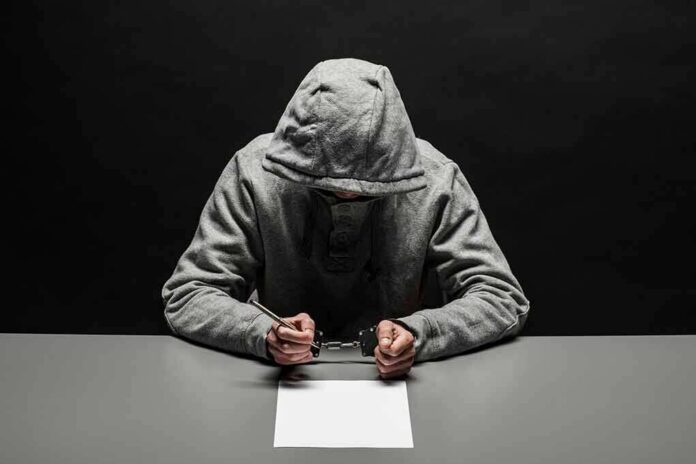 shutterstock_1074311507 Person in gray hoodie writing while handcuffed at a table