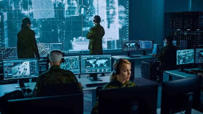 shutterstock_1936992886-5 Military analysts monitor data on multiple screens in a command center