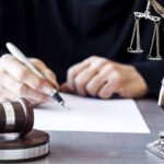 Judge writing at desk with gavel and Lady Justice statue