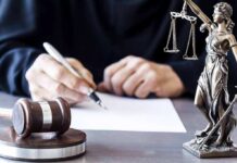 Judge writing at desk with gavel and Lady Justice statue