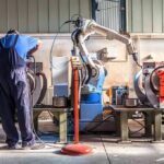 Factory worker operates near an industrial robot arm in a workshop