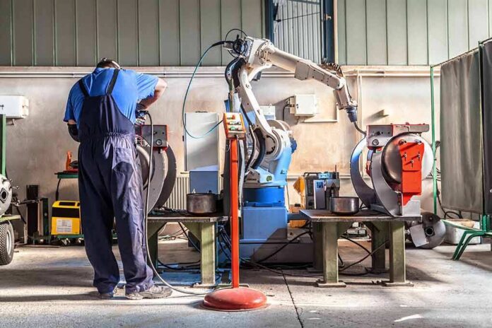 Factory worker operates near an industrial robot arm in a workshop