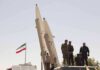 soldiers stand beside large missiles at outdoor display