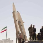 soldiers stand beside large missiles at outdoor display