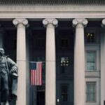 Statue in front of a neoclassical government building with columns and a U.S. flag