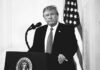 Viral Lion Montage Sparks Instant Backlash Donald Trump at a podium with microphone and U.S. flag in background