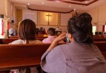 Church Sting Roils Talarico Bid people seated in church pews facing a cross