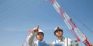 Two construction workers reviewing plans at a site with cranes