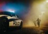 Street Takeover Chaos Explodes Police car with flashing lights at night as two people run in a foggy alley
