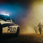 Street Takeover Chaos Explodes Police car with flashing lights at night as two people run in a foggy alley