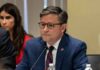 Impeach Fight Erupts – Speaker Pulls The Plug man in a blue suit speaking into a microphone at a meeting