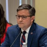 Impeach Fight Erupts – Speaker Pulls The Plug man in a blue suit speaking into a microphone at a meeting