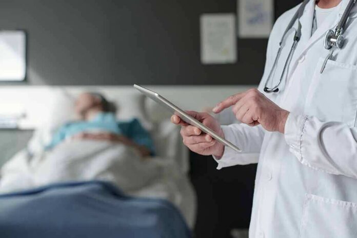 shutterstock_2316812635 Doctor using tablet beside hospital patient