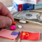 Hand picking an orange pill beside US and China flags and cash