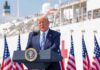SHOCKING Memo Guts Endangered Protections man in suit speaking at a podium with flags and a ship behind