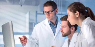 Scientists in lab coats reviewing data on a computer