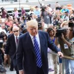 Donald Trump walks up steps through a crowd as A. J. Calloway films nearby
