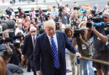 Donald Trump walks up steps through a crowd as A. J. Calloway films nearby