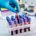 Gloved hand holding a blood sample tube in a lab rack