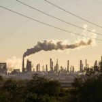 Industrial refinery with smokestack emitting plume at sunset