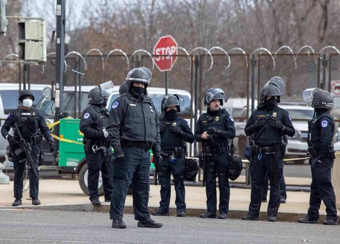 Group of police officers in riot gear standing on a street; Brian Folkerts present