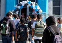Students with backpacks enter a school under a balloon arch
