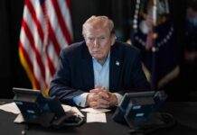 GOP Erupts After Trump Backs Attack Ad Donald Trump seated at a table between two desk phones
