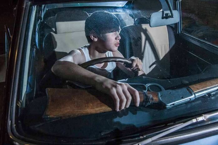 shutterstock_517847863 young man in a car holding a rifle
