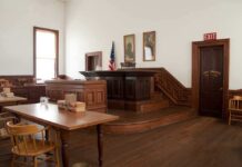 Prosecutors Allege Pattern in Russell Brand Trial Interior of a historic courtroom with wooden furniture and an American flag